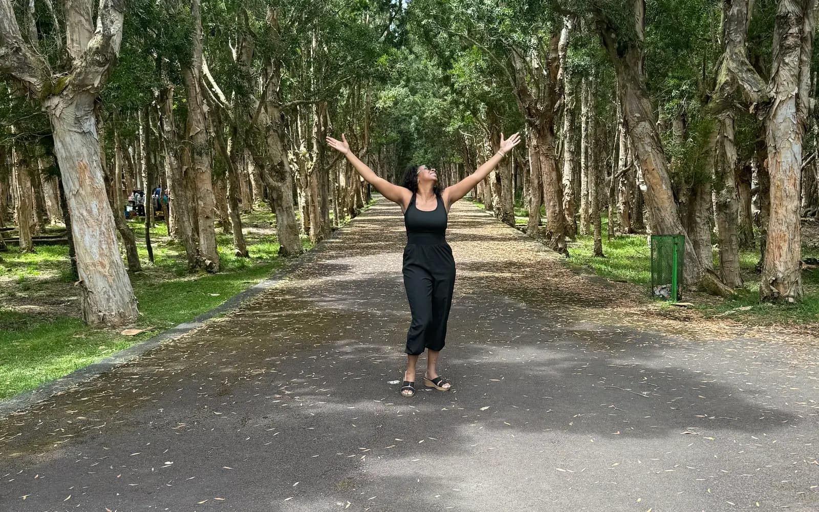 Woman with arms raised on a tree-lined path